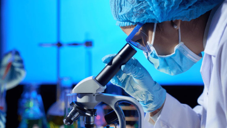 Cientista em laboratório utilizando microscópio, representando acordo entre EMBRAPII e ABIFINA para estimular a inovação em biotecnologia e química fina.