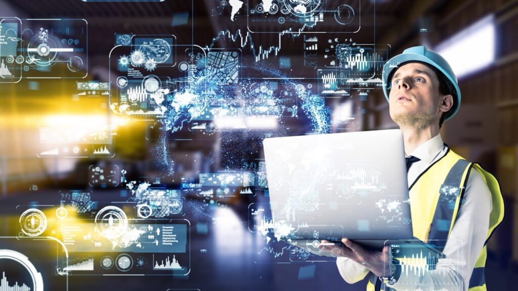 Engenheiro com capacete usando laptop em fábrica com interfaces digitais, simbolizando parceria Brasil–Alemanha para acelerar a inovação industrial.
