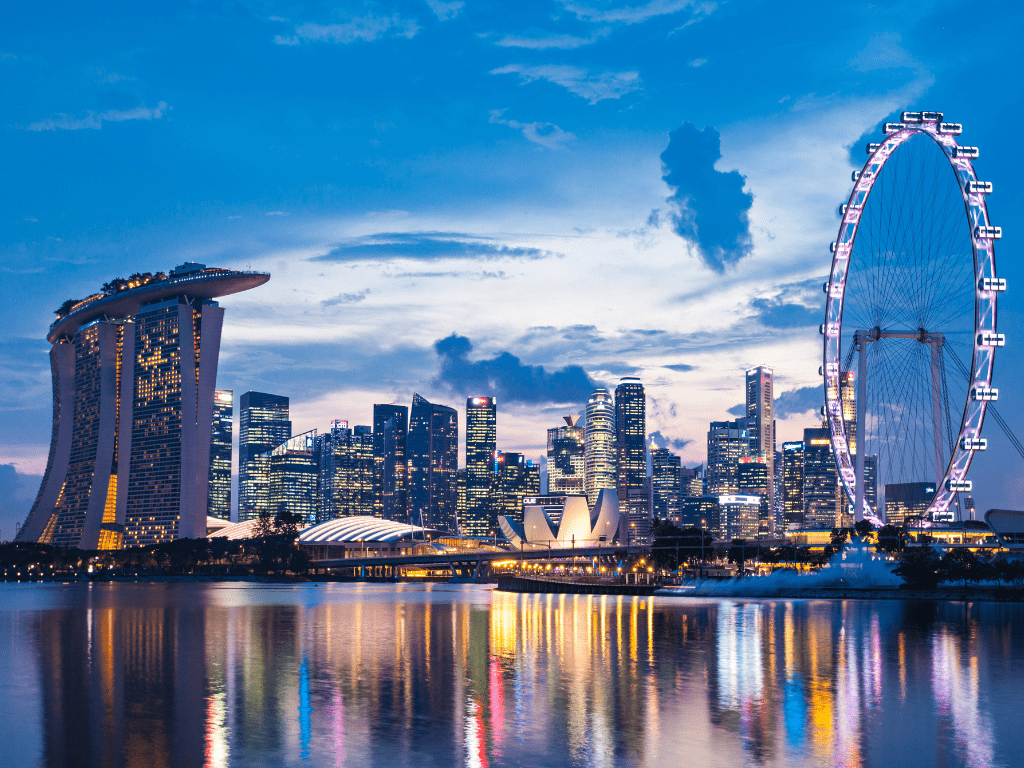 Vista panorâmica noturna de Singapura, com a Marina Bay Sands, a roda-gigante Singapore Flyer e arranha-céus iluminados.