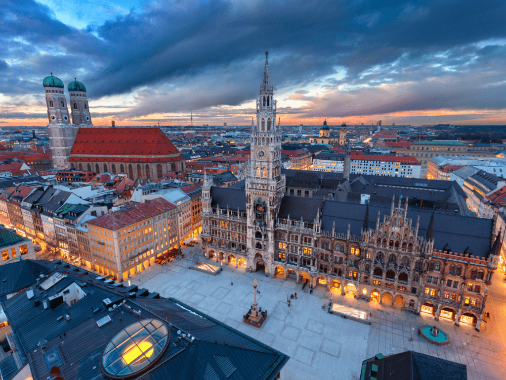 Vista aérea da Marienplatz em Munique, Alemanha, com a Nova Prefeitura (Neues Rathaus) e a Frauenkirche ao entardecer.