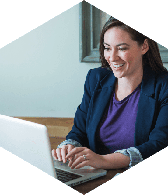 Mulher sorridente trabalhando no notebook em ambiente de escritório, usando blazer azul, transmitindo profissionalismo e produtividade.