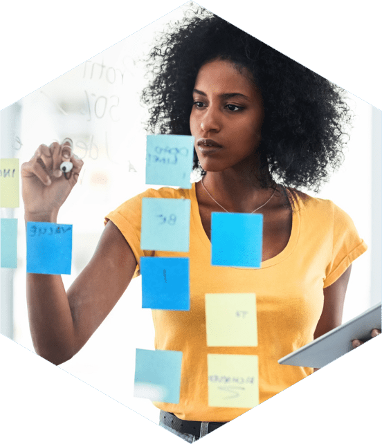 Mulher fazendo anotações em mural de vidro com post-its coloridos durante uma sessão de brainstorming.