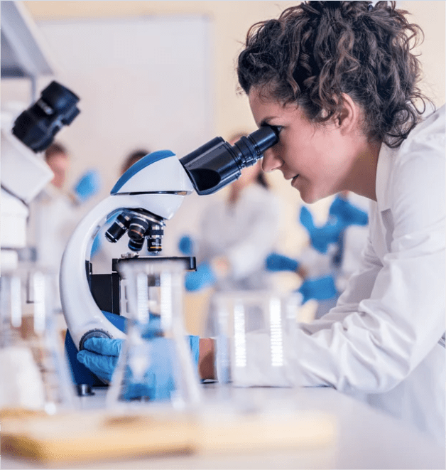 Pesquisadora em laboratório usando microscópio — bolsas de pesquisa e fomento à inovação.