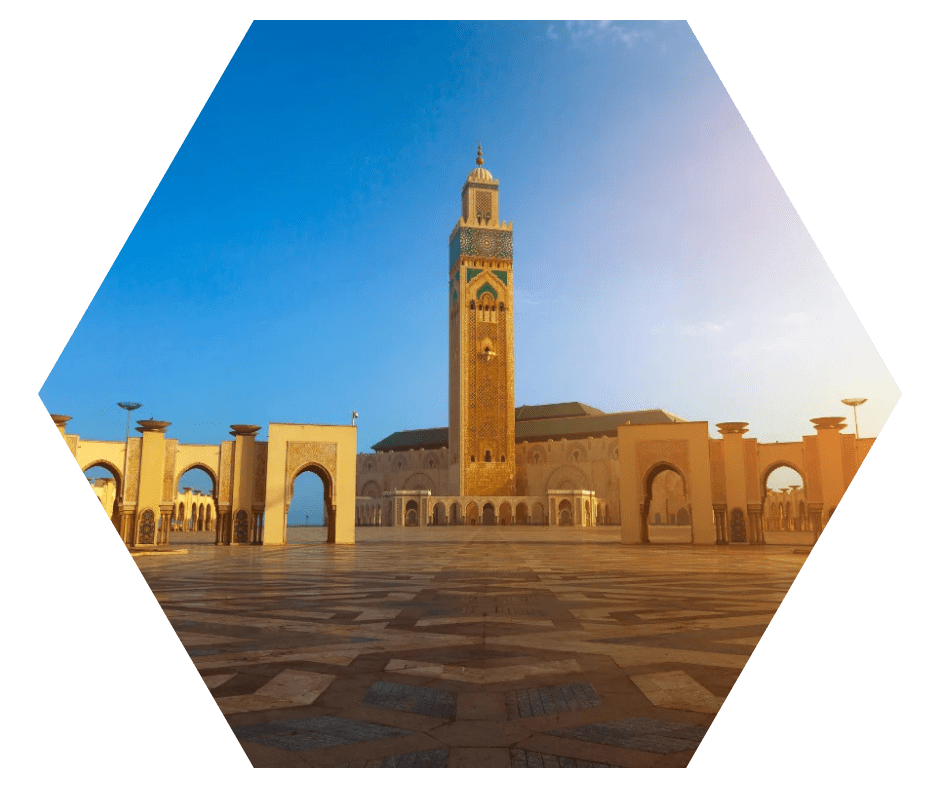 Vista frontal da Mesquita Hassan II, com minarete e arcos iluminados pela luz dourada do fim de tarde em Casablanca, Marrocos.