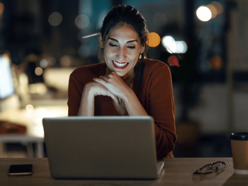 Profissional sorrindo diante do notebook à noite em escritório; conceito de automatizar e organizar a jornada na Lei do Bem