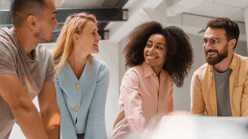 Colaboradores conversam sorrindo em uma mesa de trabalho — exemplo de cultura de inovação no ambiente corporativo.