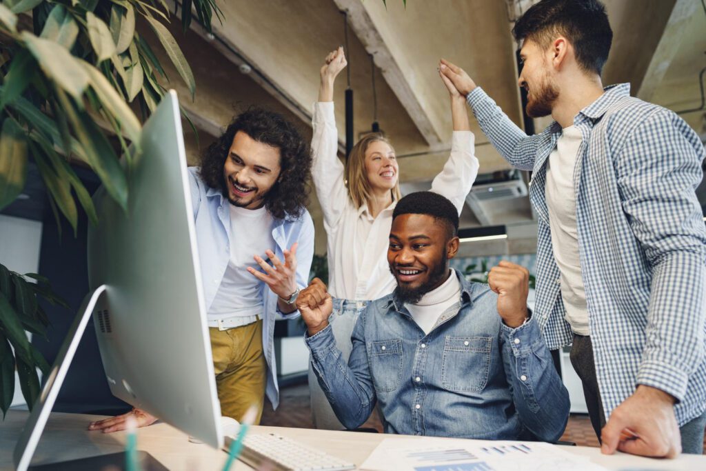 Equipe celebra resultados em frente ao computador, simbolizando cultura para inovação e sucesso da transformação